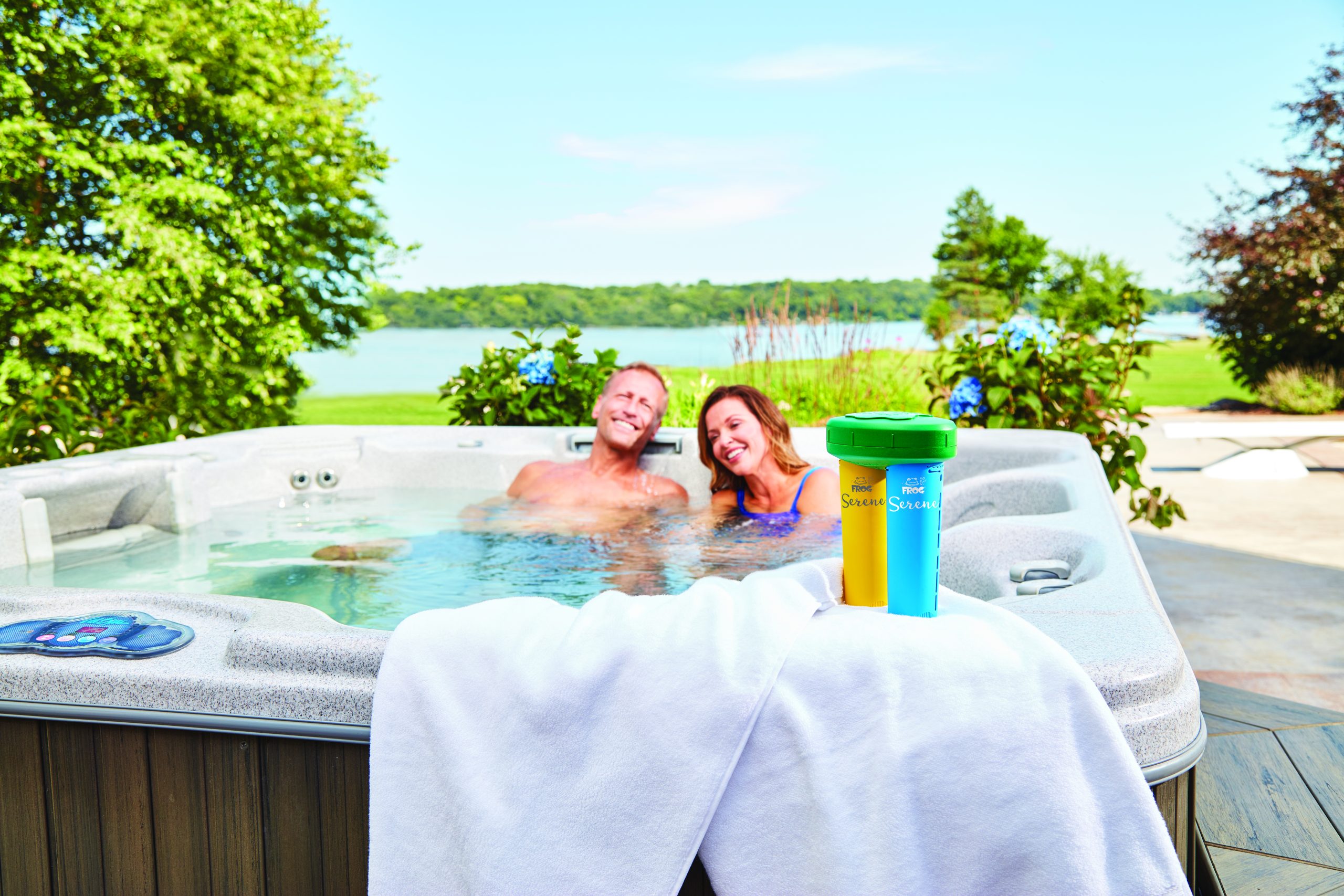 Image of a couple smiling while in a hot tub. The FROG Serene floating system is sitting on the side of the spa on top of a white towel.
