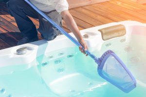 Image of a man bending over a hot tub using a strainer to get organic matter out of the spa.