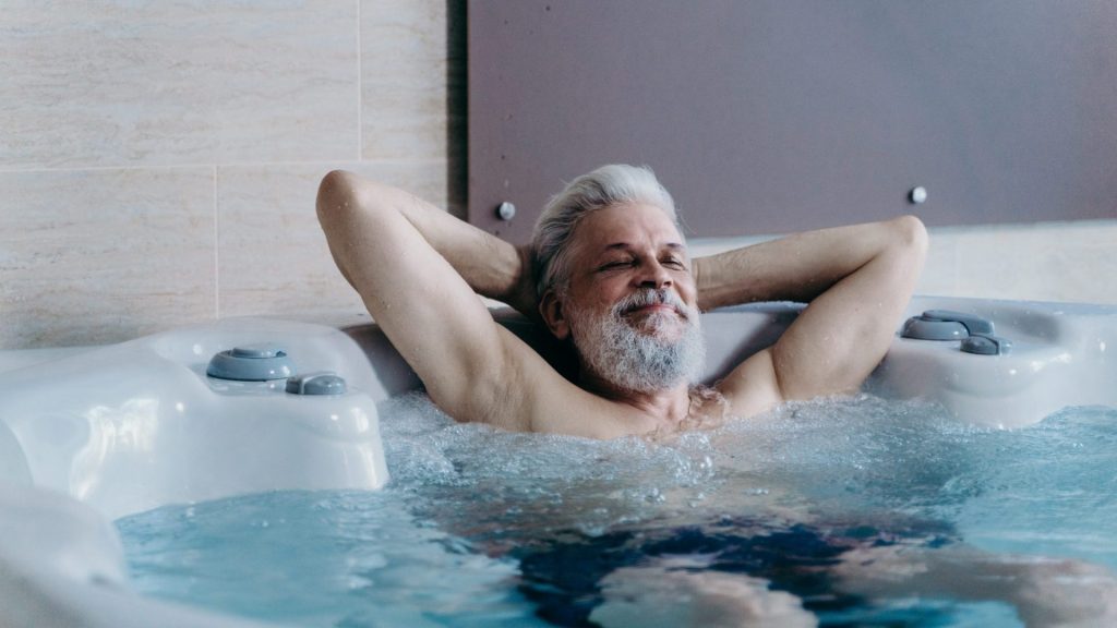 An older gentleman reclining in the hot tub with his eyes closed.