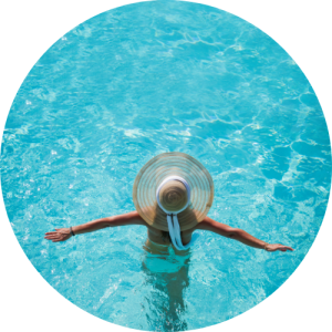 Person in sun hat swimming in pool with crystal clear water
