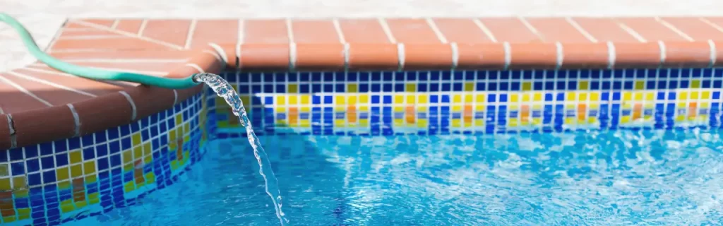 A garden hose filling up an outdoor pool.