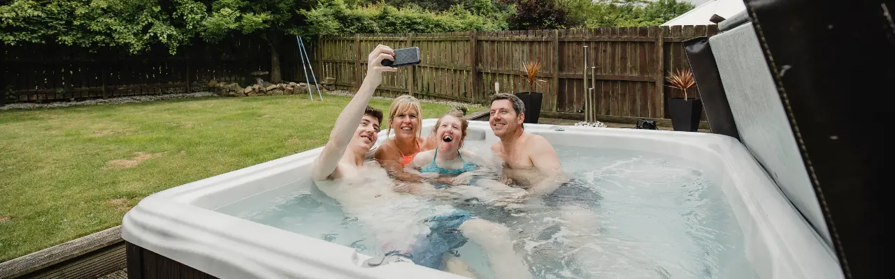 A family poses for a selfie in the hot tub. A hot tub cover is sitting to the right of the hot tub propped up.