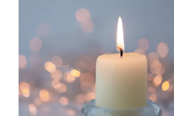 A white candle burns. In the background a winter scene is blurred out.