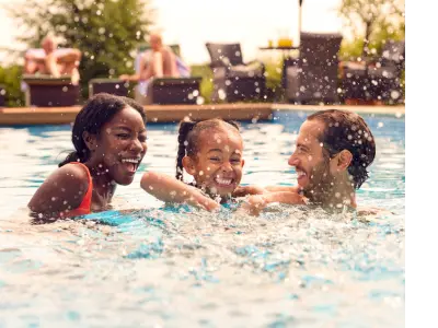 An interracial family splashes in their outdoor pool.